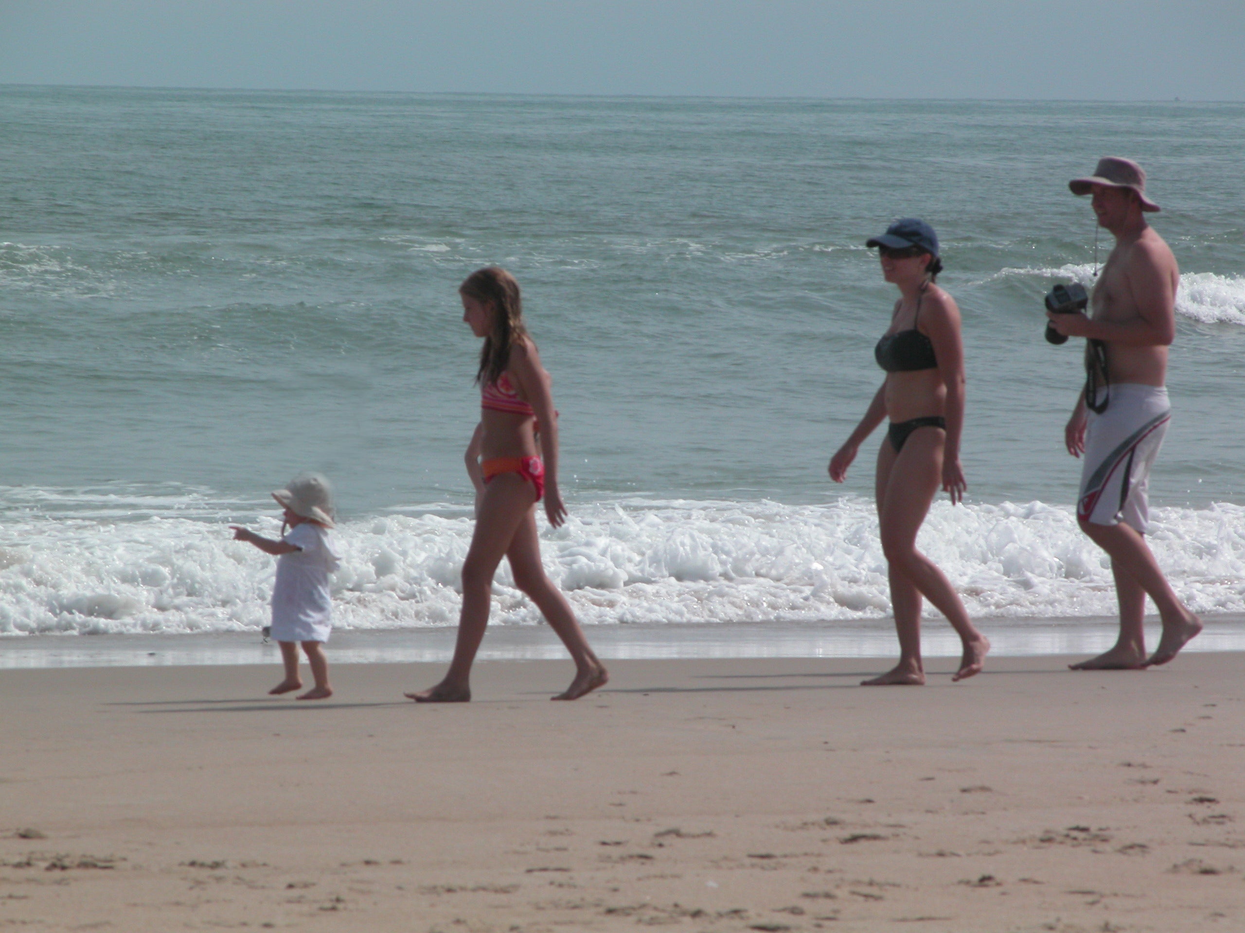 Toddler walking down the beach with sister and mom in tow
